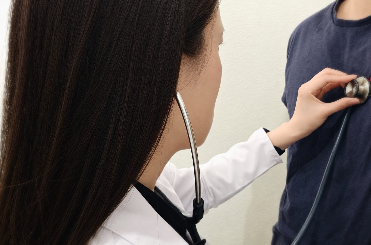 A clinician in a white coat listening to a patient's heart with a stethoscope.